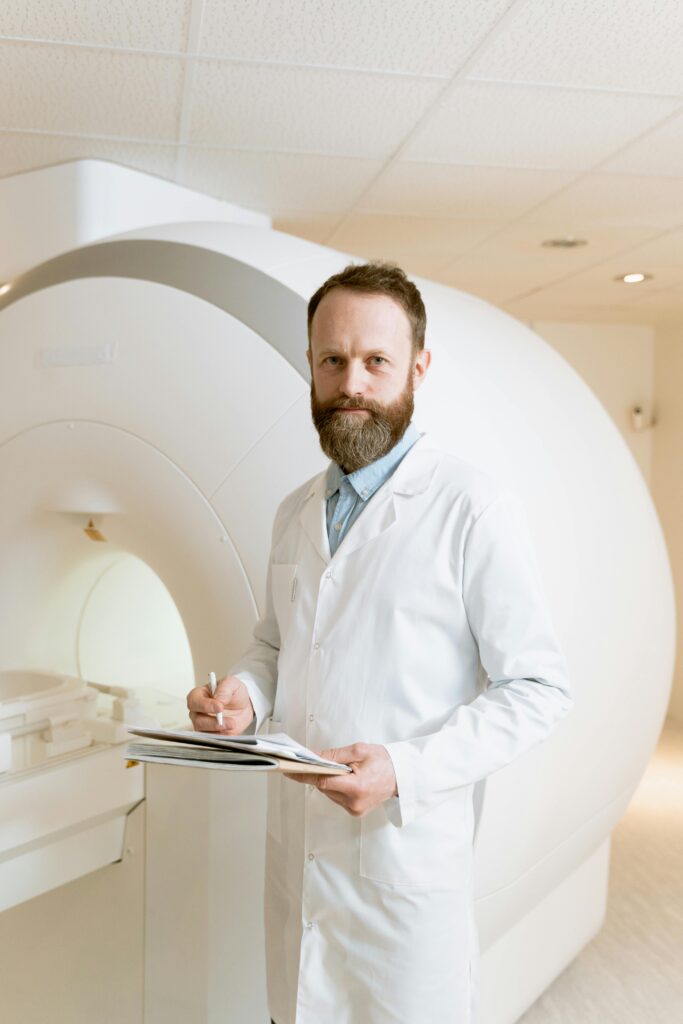 Experienced doctor in a hospital, standing by an MRI scanner, holding documents and smiling.